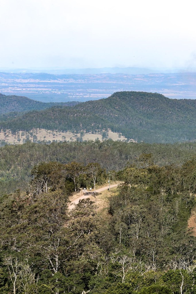 A panoramic view of rolling hills and mountains covered with dense greenery, overlooking a distant valley and sky.